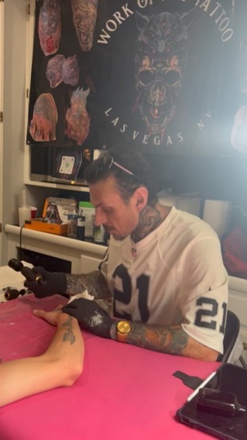 Joshua Cole tattoos black-grey rose on forearm beneath Work of Art Las Vegas banner — Joshua Cole offsite booking, Work of Art Las Vegas
