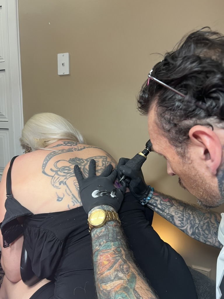 Joshua Cole tattoos upper back beside faded blue portrait on blonde client offsite — Joshua Cole offsite booking, Work of Art Las Vegas