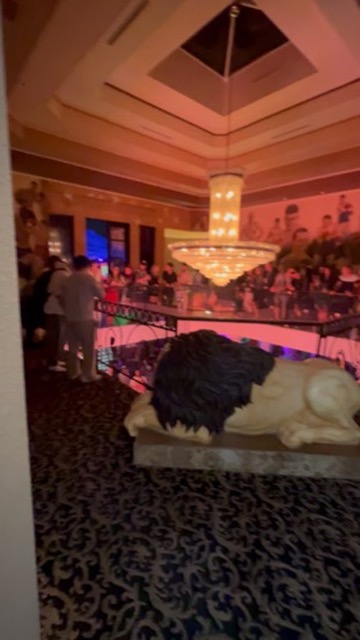 Crowd gathers on balcony above lion statue beneath crystal chandelier at Vegas venue — Joshua Cole offsite booking, Work of Art Las Vegas