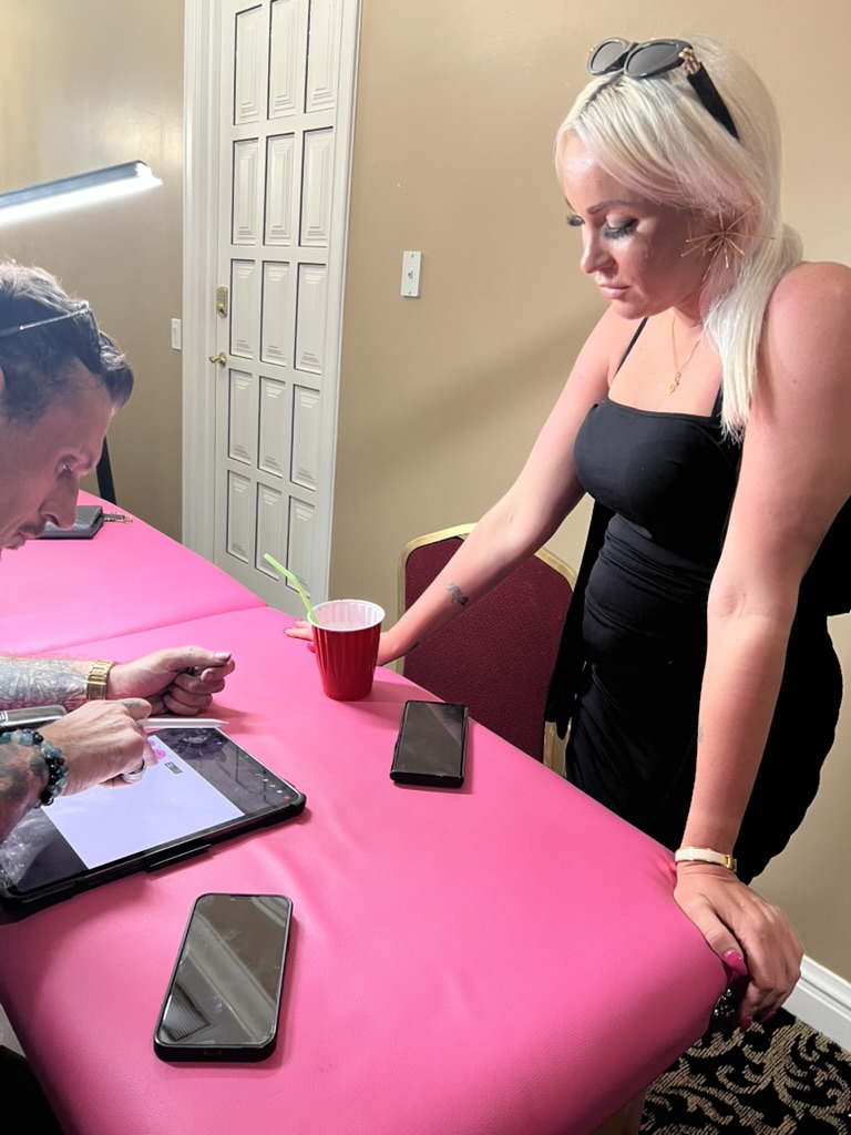 Blonde client watches Joshua Cole draw tattoo design on tablet — Joshua Cole offsite booking, Work of Art Las Vegas