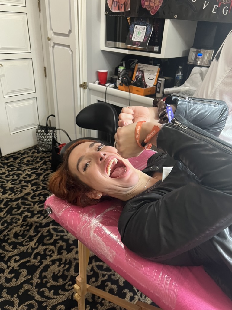 Red-haired client laughs on pink-wrap table wearing orange Stacks wristbands — Joshua Cole offsite booking, Work of Art Las Vegas