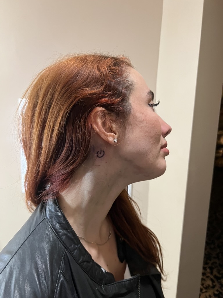 Fresh black power-button neck tattoo behind red-haired client's ear, finished offsite — Joshua Cole offsite booking, Work of Art Las Vegas
