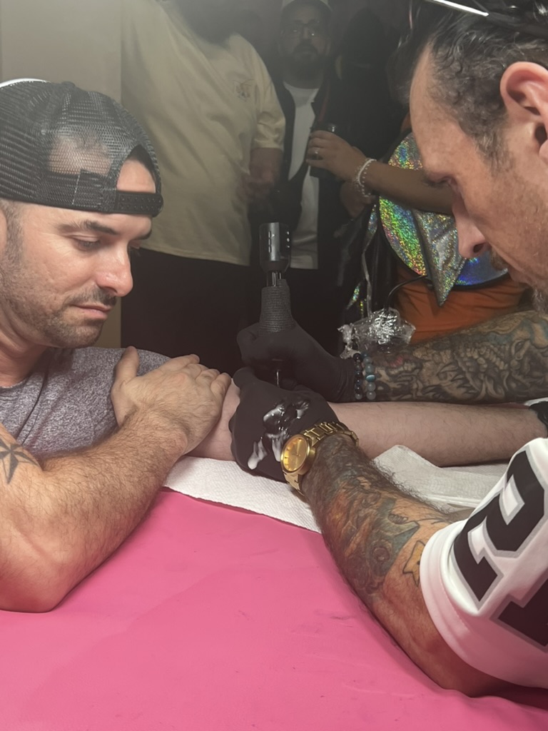 Joshua Cole tattoos client's inner forearm as onlookers watch at pink offsite station — Joshua Cole offsite booking, Work of Art Las Vegas