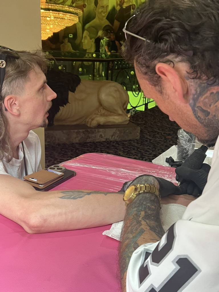 Joshua Cole tattoos forearm on pink table beside lion statue and boxing mural offsite — Joshua Cole offsite booking, Work of Art Las Vegas