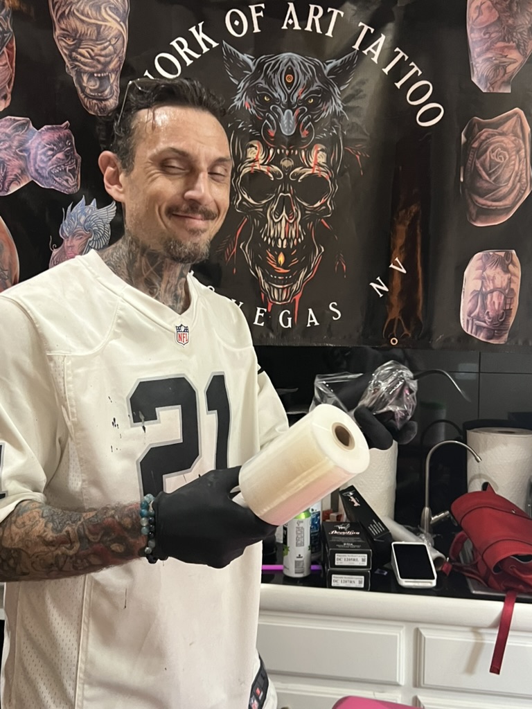 Joshua Cole smiles holding barrier film and wrapped machine at WOA banner — Joshua Cole offsite booking, Work of Art Las Vegas
