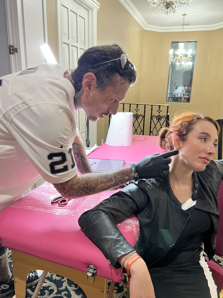Joshua Cole marks neck spot behind client's ear at pink portable table — Joshua Cole offsite booking, Work of Art Las Vegas