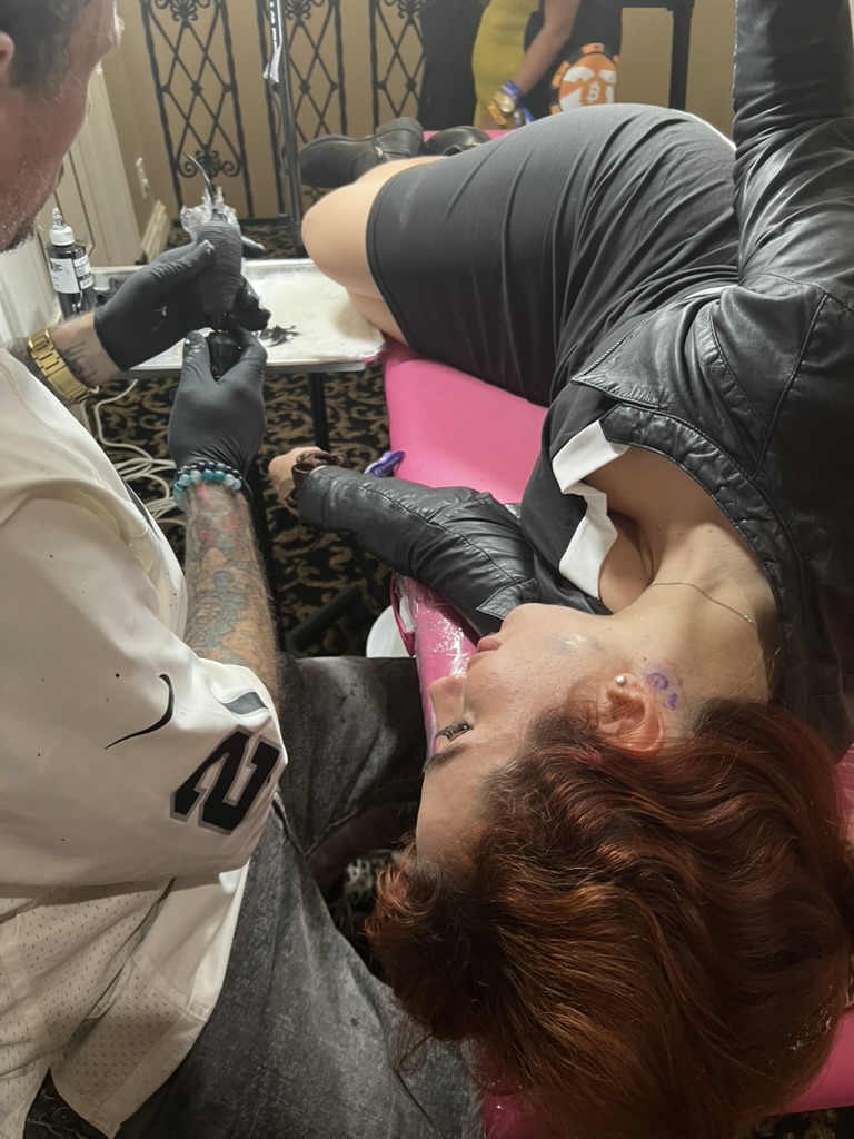 Joshua Cole tattoos neck on client lying on pink plastic-wrapped table — Joshua Cole offsite booking, Work of Art Las Vegas