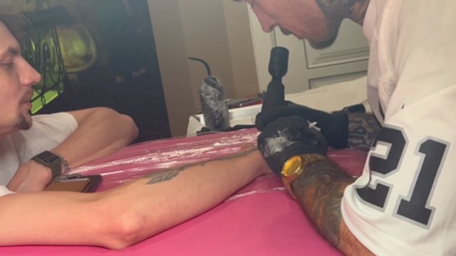 Raiders jersey artist tattoos rose on forearm at pink-covered offsite table — Joshua Cole offsite booking, Work of Art Las Vegas