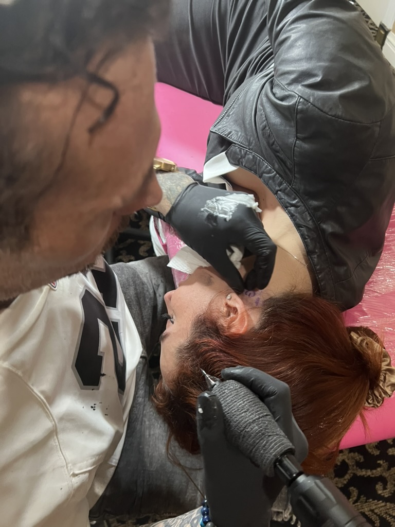 Joshua Cole tattoos purple script behind client's ear on pink-wrapped offsite station — Joshua Cole offsite booking, Work of Art Las Vegas