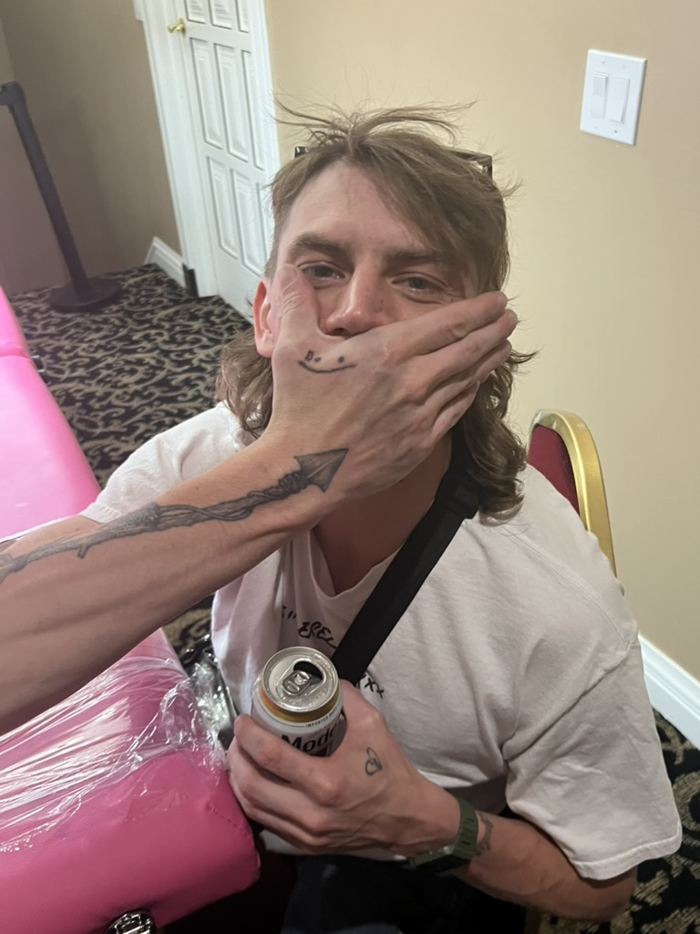 Smiley finger tattoo covers man's mouth; spear forearm and heart hand at offsite — Joshua Cole offsite booking, Work of Art Las Vegas