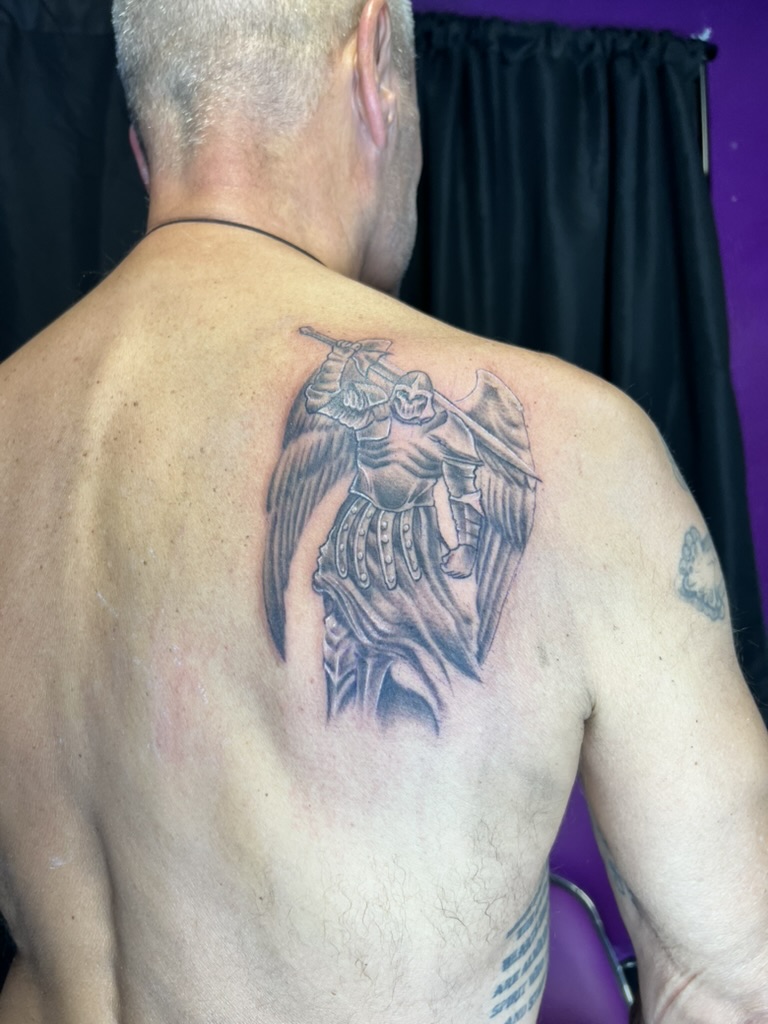 Detailed black and grey armored archangel with feathered wings on shoulder blade. — Joshua Cole, Work of Art Las Vegas