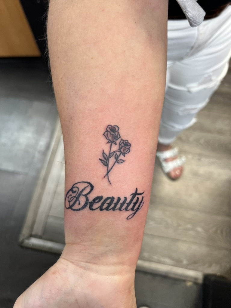 Cursive Beauty script with crossed rose stems on inner forearm. — Joshua Cole, Work of Art Las Vegas