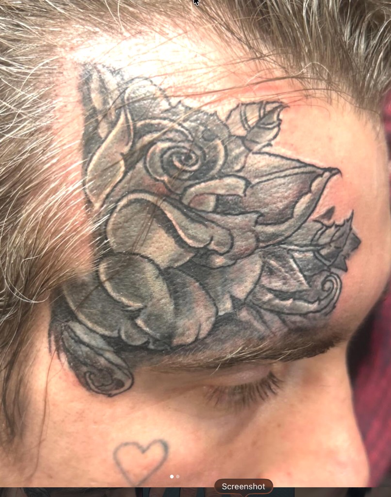 Soft-shaded black-grey rose tattoo on temple beside a small outline heart on cheek — Joshua Cole, Work of Art Las Vegas