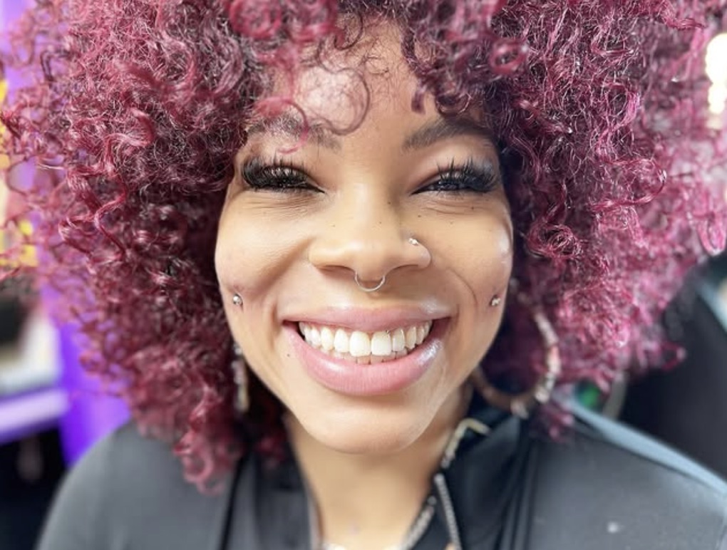 Smiling client with magenta curls, septum ring, nostril stud and cheek piercings — Joshua Cole, Work of Art Las Vegas