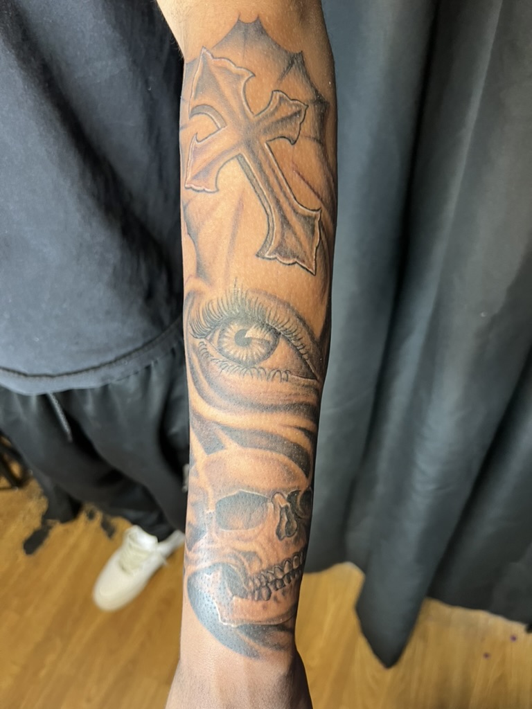 Ornate cross, realistic eye, and skull stacked down outer forearm. — Joshua Cole, Work of Art Las Vegas