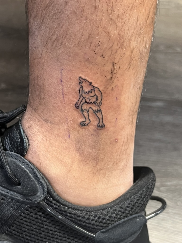 Fine-line howling werewolf outline tattooed above the ankle on lower leg. — Joshua Cole, Work of Art Las Vegas