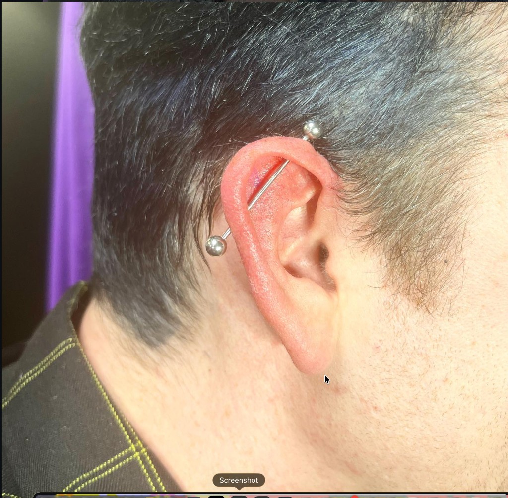 Silver industrial barbell through upper helix cartilage on short-haired client ear — Joshua Cole, Work of Art Las Vegas