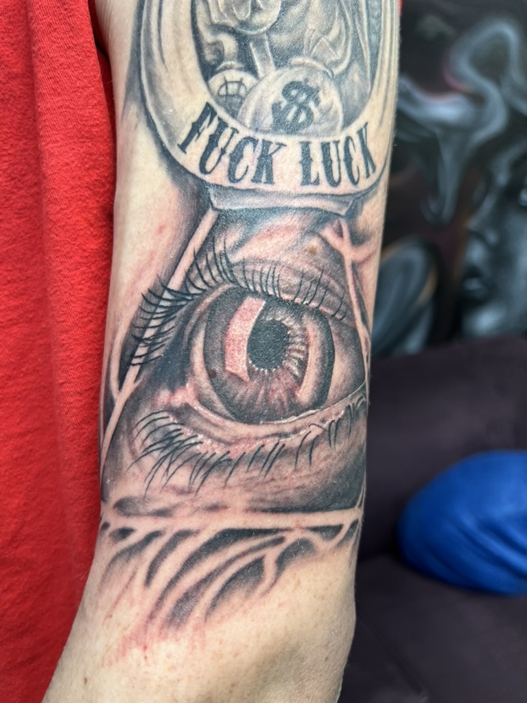 Realistic all-seeing eye with FUCK LUCK banner on outer bicep. — Joshua Cole, Work of Art Las Vegas
