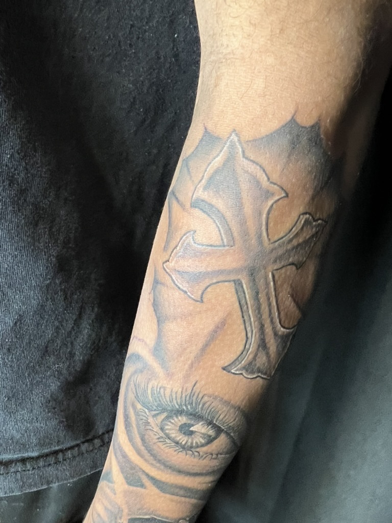 Beveled ornate cross above a realistic eye on outer forearm. — Joshua Cole, Work of Art Las Vegas