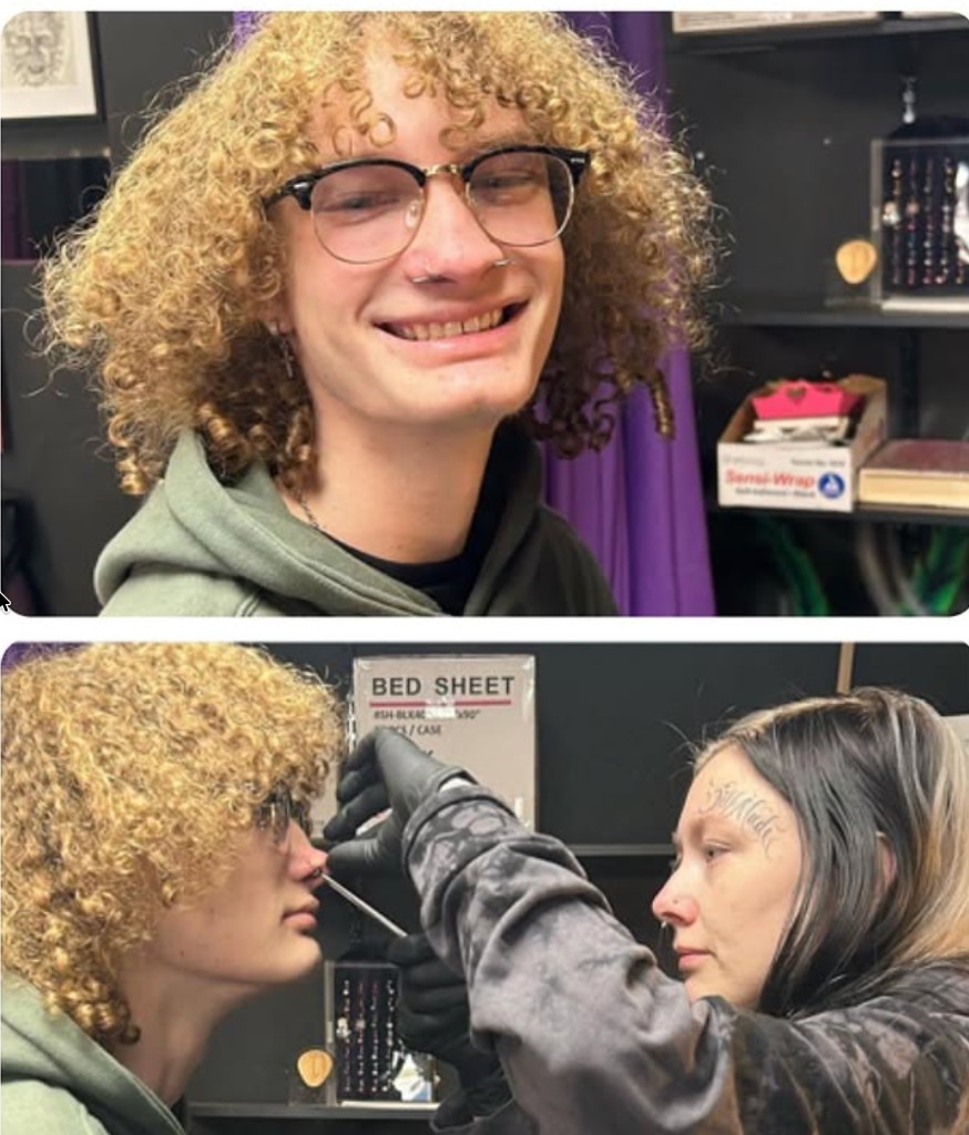 Curly-haired client smiling after septum ring as piercer needles the columella below — Joshua Cole, Work of Art Las Vegas
