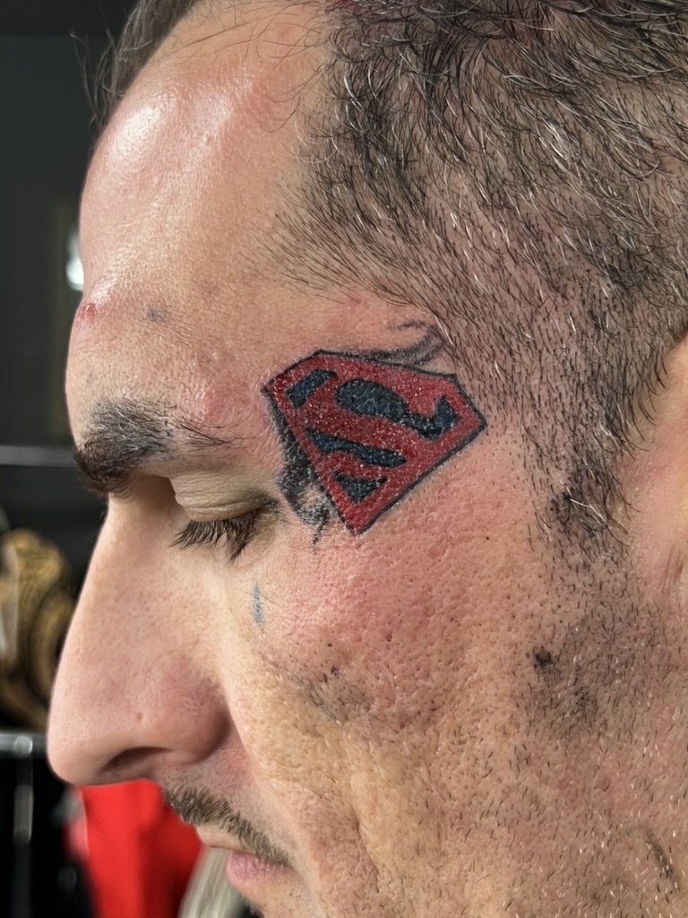 Red and black Superman S shield tattoo on a man's left temple. — Joshua Cole, Work of Art Las Vegas